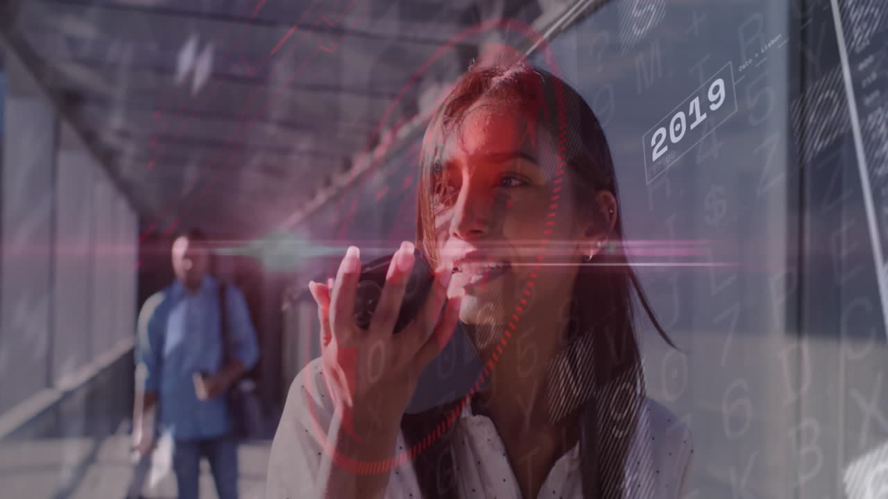 Woman speaking into smartphone in skybridge, showing red technology interface with numeric codes