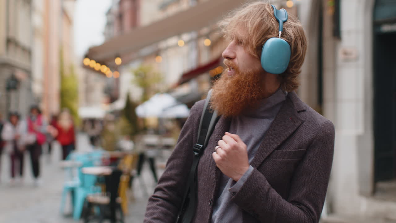 Happy young man in wireless headphones choosing listening music in smartphone dancing outdoors