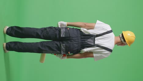 full body of back view asian man painter wearing safety helmet standing and look around in the green screen background studio