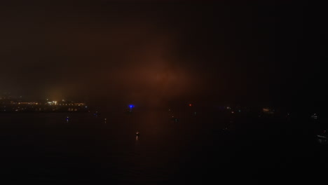 lights from fireworks glow in the sky on a foggy fourth of july - aerial flyover