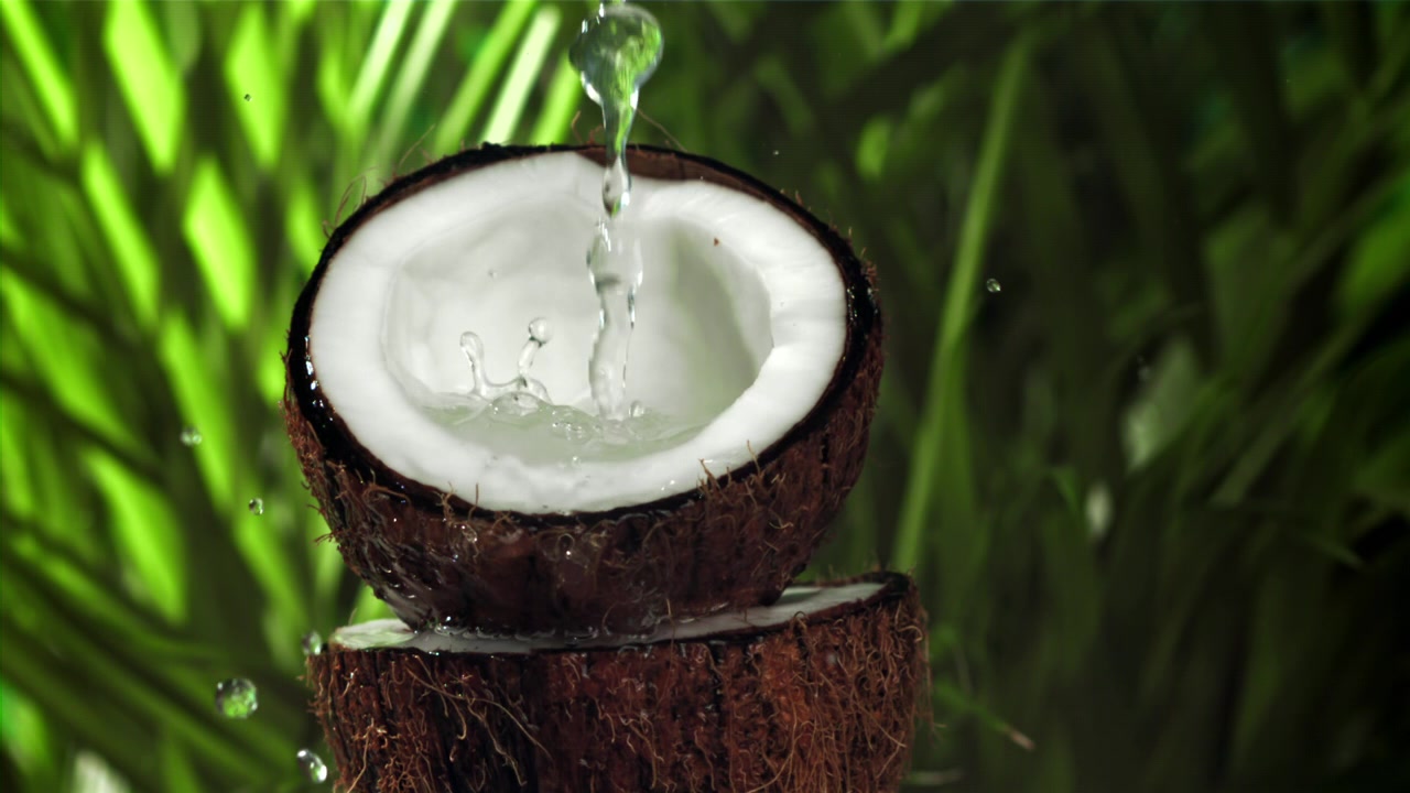 Refreshing Water Pours into a Halved Coconut in Slow Motion