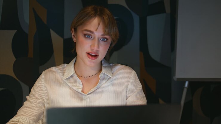 Primo piano di una donna felice che lavora fino a tardi in ufficio e consulta contenuti online. Videochiamata di lavoro a tarda ora