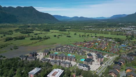 Aerial pan over green fields, mountains, and modern residential condos in southern Chile near Pucón. Scenic valley landscape with a village in view