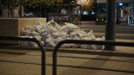 piled sandbags line a tram station at night, offering protection in an urban area