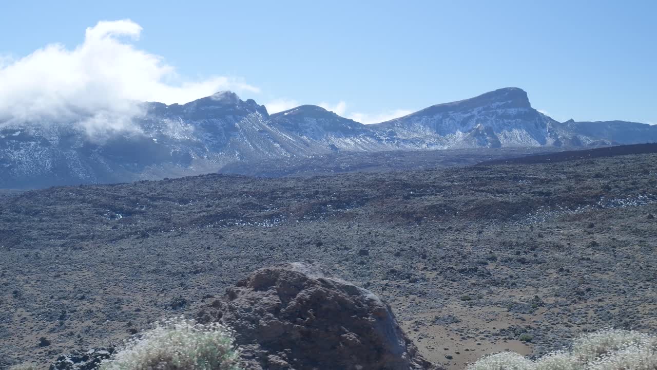 Panoramica scenografica di un paesaggio vulcanico arido con montagne innevate