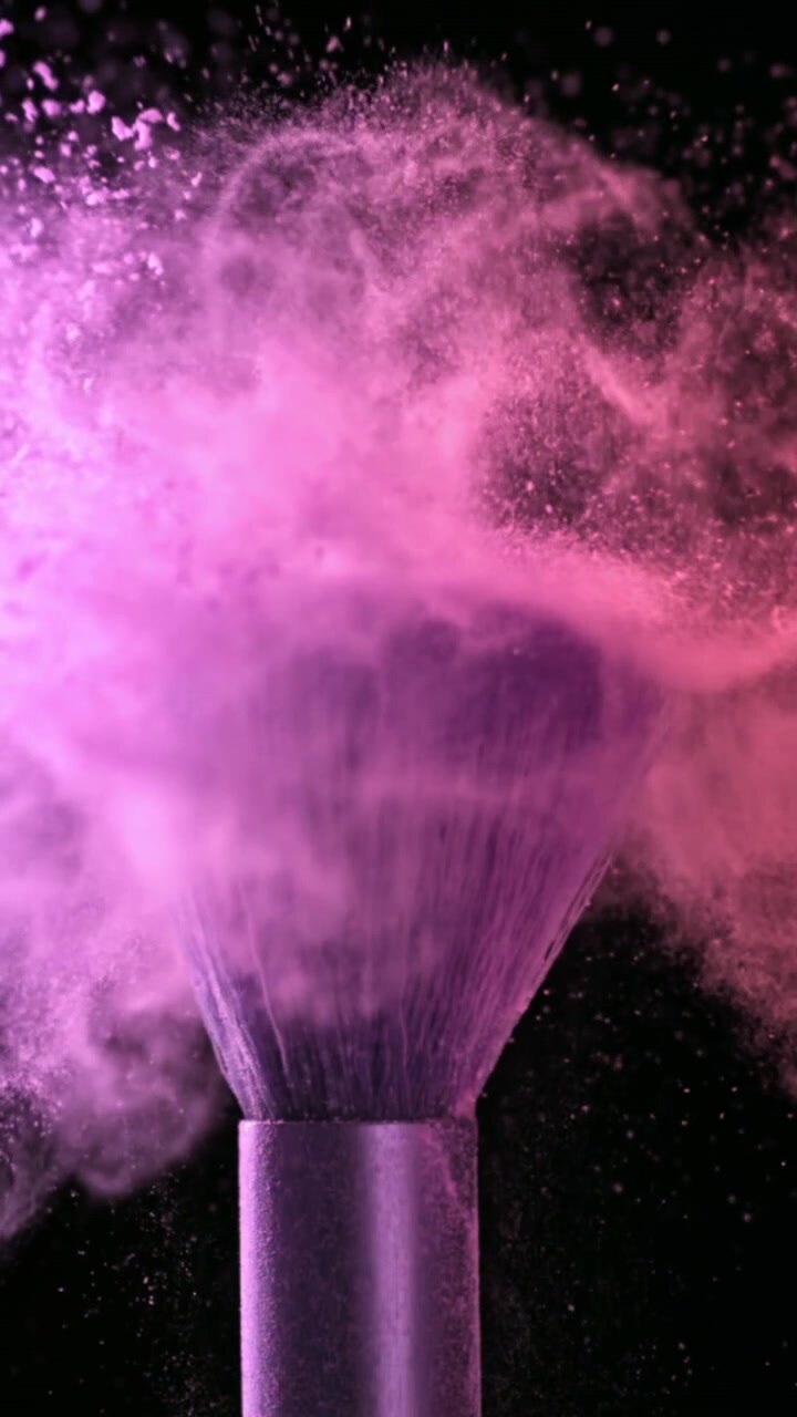Movimento rallentato di polvere cosmetica rosa e viola che si disperde da un pennello da trucco