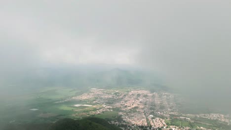 small mexican town surrounded by farmland slowly emerges through dense clouds near tuxpan, mexico on a rainy day. slow motion drone aerial