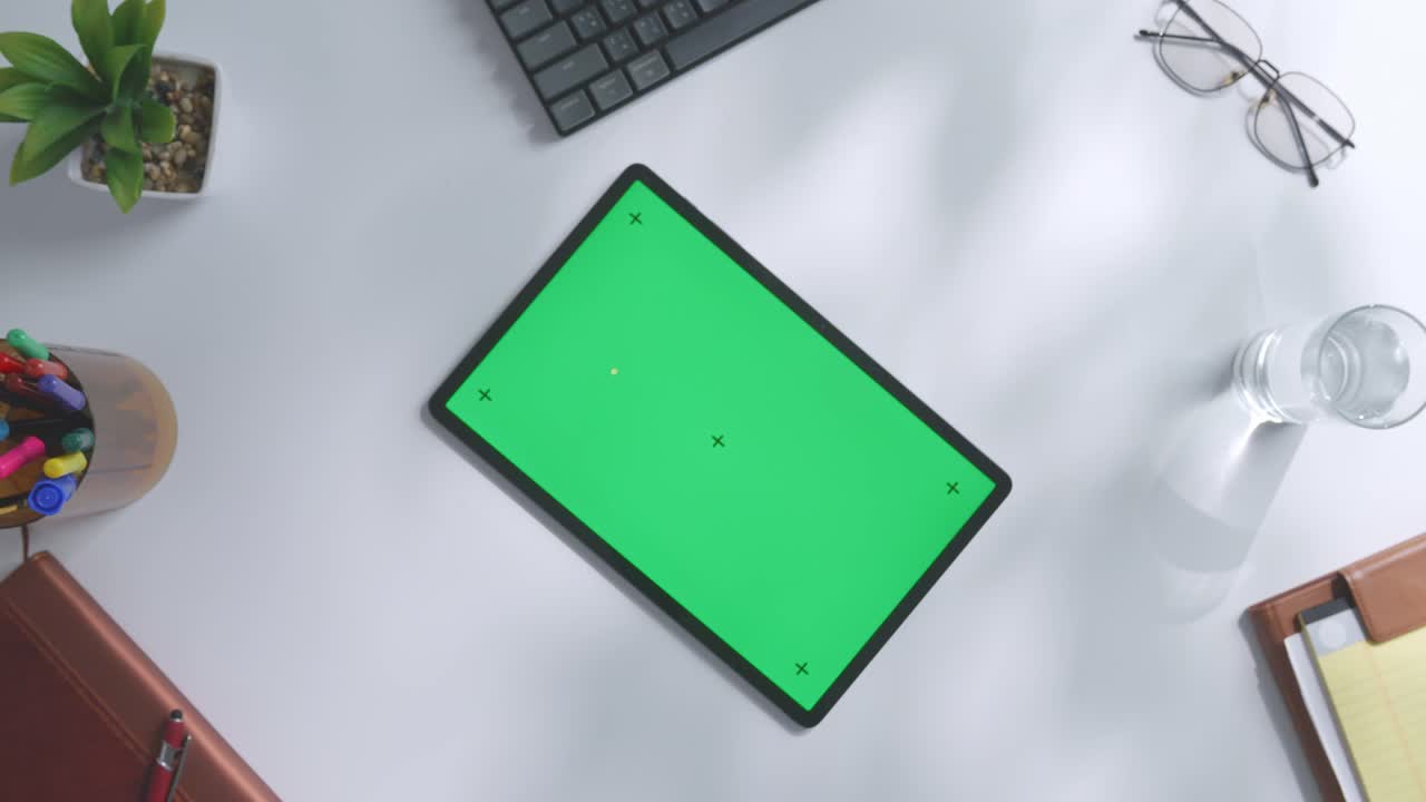 vista de arriba hacia abajo de una computadora portátil con pantalla verde simulada pantalla chromakey en un escritorio de oficina de madera al lado de la libreta con bolígrafos, gafas y un vaso de agua.