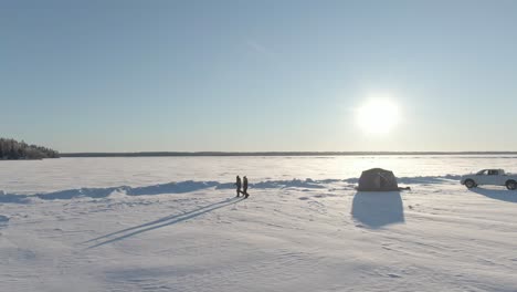 2 women walking away from tent ice fishing on a frozen lake, tundra, drone