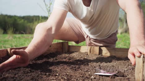 man digging soil to plant seeds on wooden planter