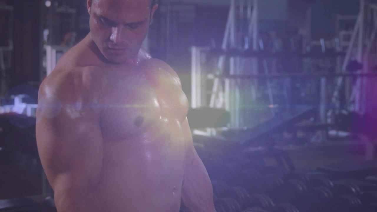 Uomo a torso nudo che impugna un bilanciere EZ ed esegue curl in palestra, allenando i bicipiti, con un bagliore dell'obiettivo.