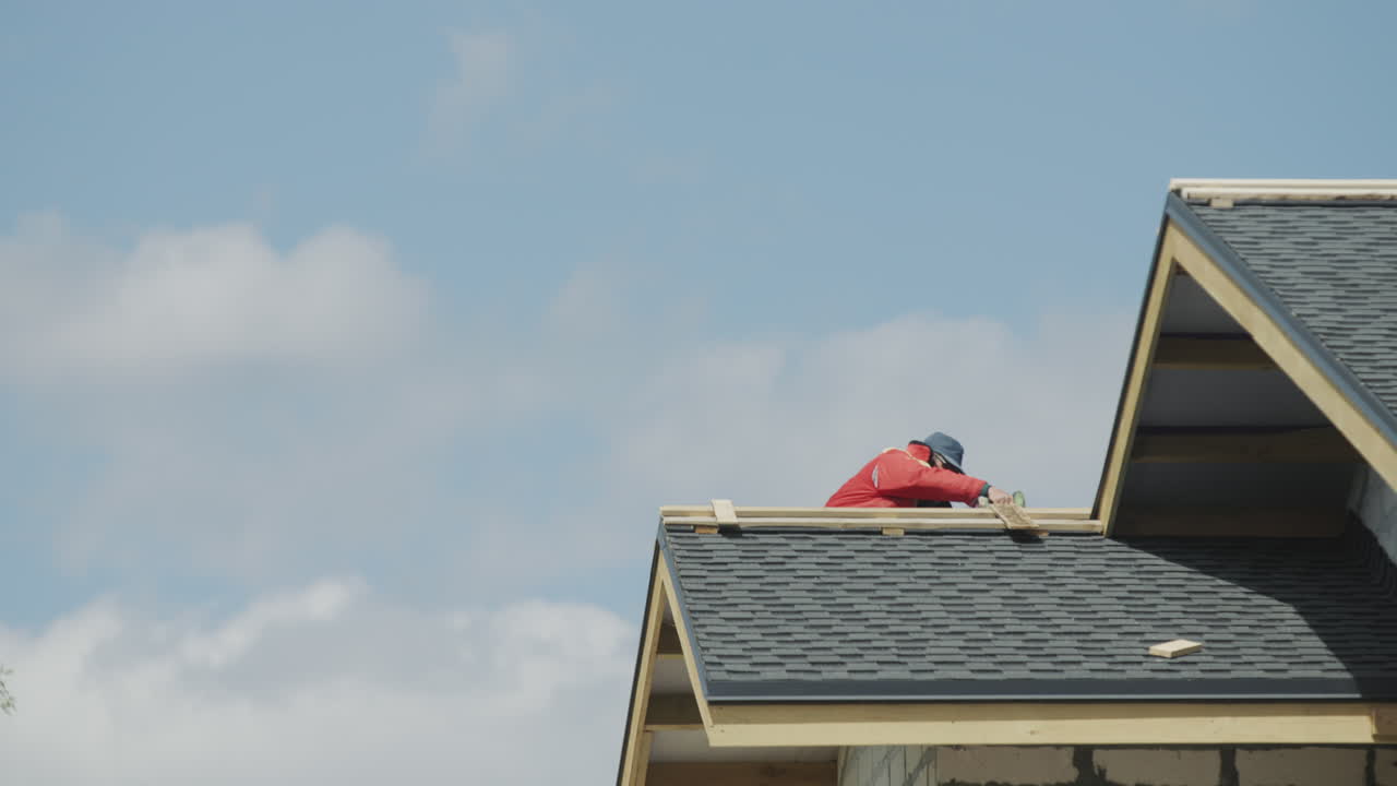 The builder is working on the roof of the house - laying shingles.
