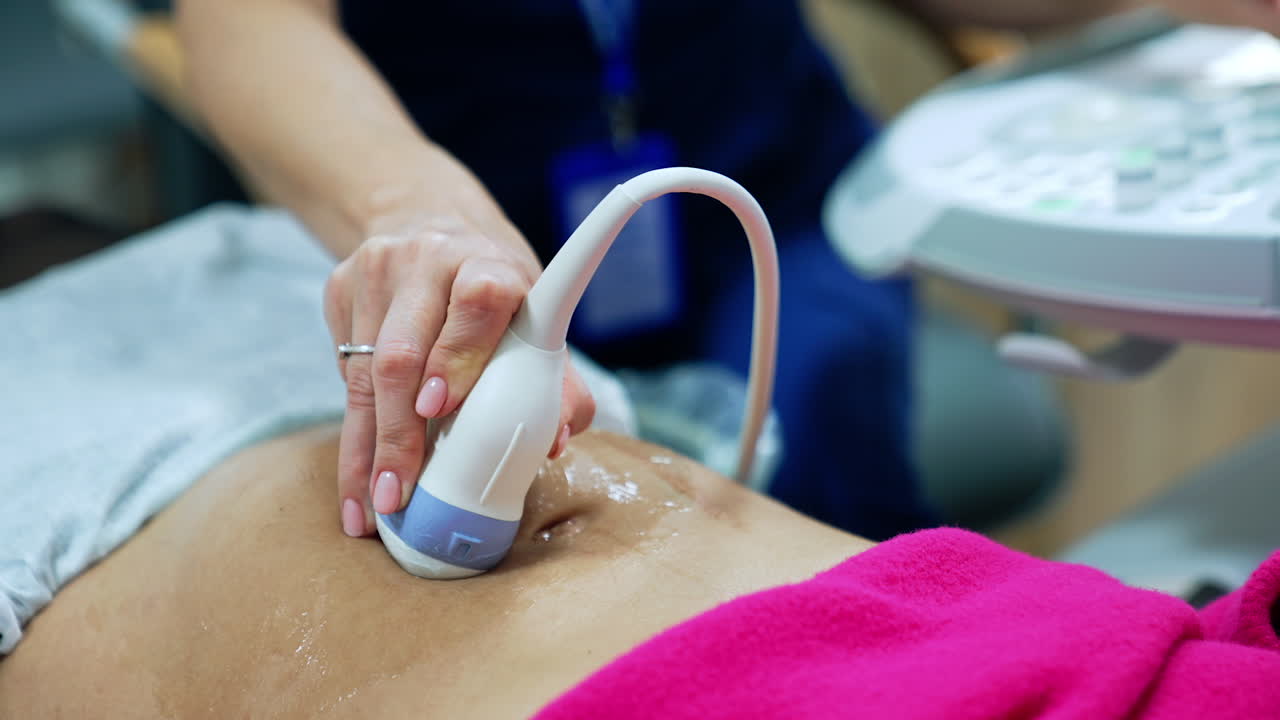 Obstetrician holds the ultrasound device on the patient's pregnant belly. Woman is checked in the clinics. Close up.