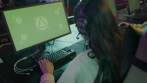 rear view of a female gamer playing virtual video games on professional powerful computer with green screen display