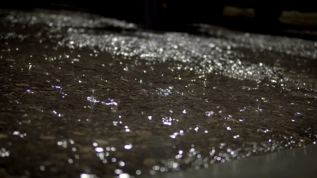 Large drops of rain fall on wet asphalt road in the night city, cinematic background loop with selective focus