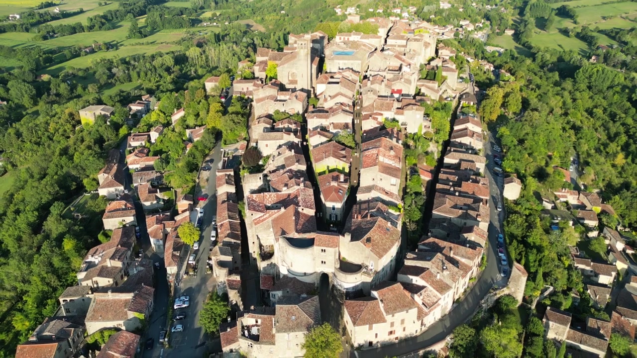 Vista aerea con drone nella campagna francese di una piccola e antica città medievale in mattoni sulla cima di una montagna circondata da campi verdi, sorvolando all'indietro in una giornata di sole a Cordes Sur Ciel