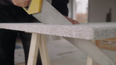 man using a handsaw to cut an acoustic panel for the ceiling house renovation diy sawdust