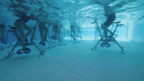 vista submarina de personas en bicicleta acuática en una piscina en cámara lenta