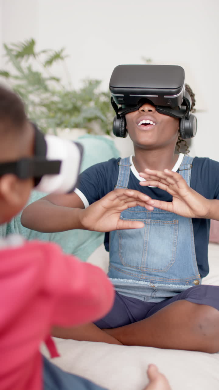 Vertical video of african american sister and brother using vr headset in living room, slow motion