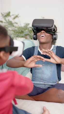 vertical video of african american sister and brother using vr headset in living room, slow motion