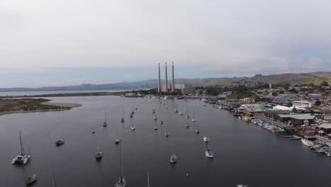 low aerial shot flying over sailboats in the harbor towards the morro bay power plant in morro bay, california