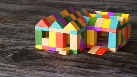 Colorful-house-being-build-from-a-pile-of-colorful-wooden-blocks.-Camera-position-pans-around-it.-Construction,-development-of-preschool-kid’s-building-imagination.-Fun-with-learning-aspects.