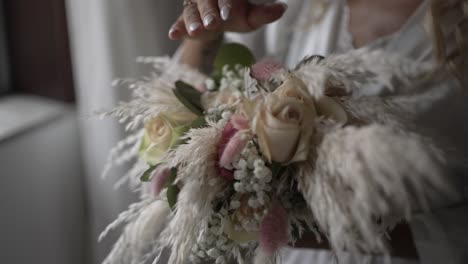 Bride's-hand-holding-a-bouquet-of-roses,-pampas-grass,-and-eucalyptus-by-a-window