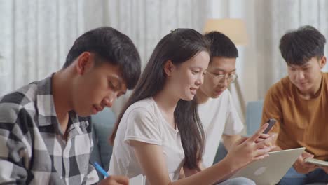 close up of asian teen group studying at home. students with books and laptop looking at smartphone, celebrating success in project, giving high five gesture