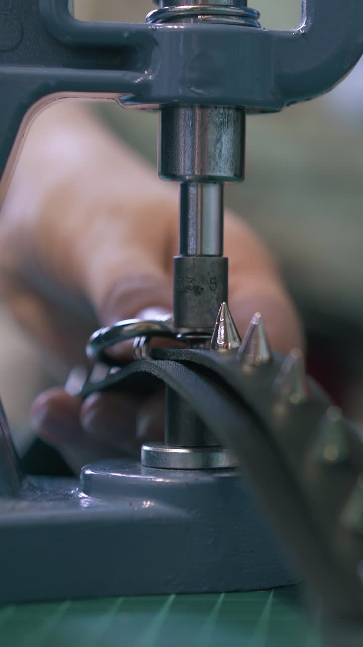 CU: Skilled tailor sets accessories on black leather belt with loop on workshop press machine extreme closeup