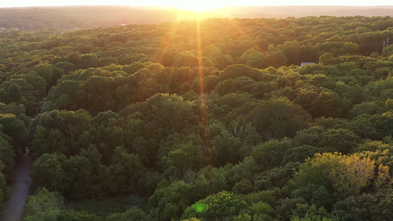 aerial flight over a rural forested area towards a bright summer sunset in the Northeastern USA, with an intense lens flare