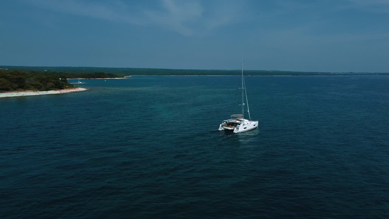 un barco de vela catamarán en una bahía azul clara junto al mar en las idílicas vacaciones en el mar mediterráneo adriático cerca de la costa croata con cielo azul
