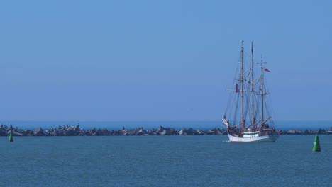 sailing vessel zawisza czarny (staysail schooner) leaves port of liepaja in hot sunny summer day, medium shot from a distance