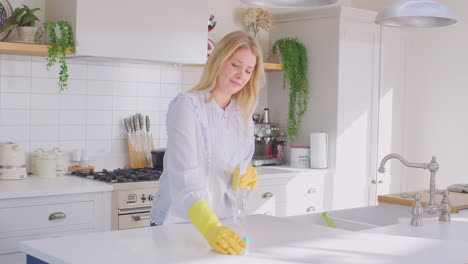 Toma-Panorámica-De-Una-Mujer-En-Casa-En-La-Cocina-Usando-Guantes-De-Goma-Limpiando-La-Superficie-De-Trabajo-Usando-Spray-De-Limpieza---Filmada-En-Cámara-Lenta