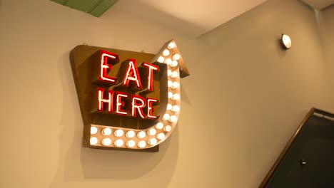 Slow motion of 'Eat Here' neon sign hanging in food court dining area