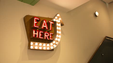 slow motion of 'eat here' neon sign hanging in food court dining area