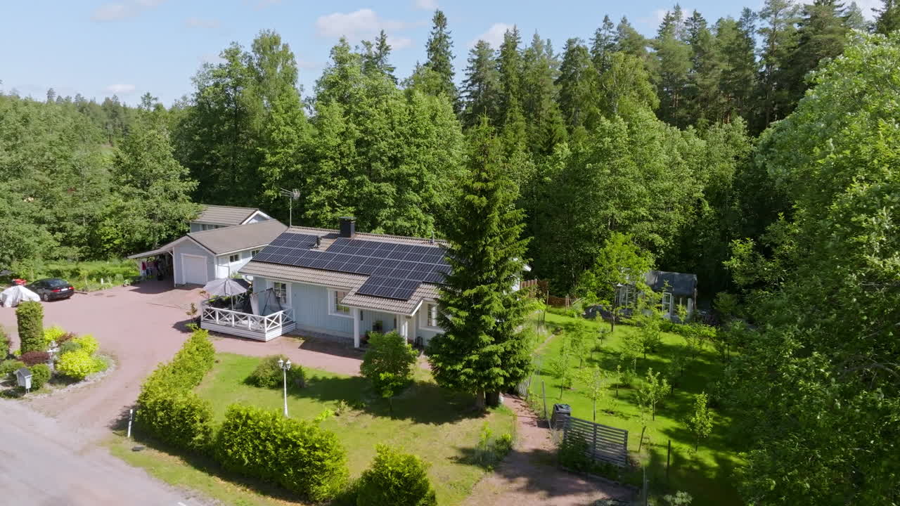 Vista aerea dietro un albero, che rivela una casa con pannelli fotovoltaici, giardino estivo fiorito