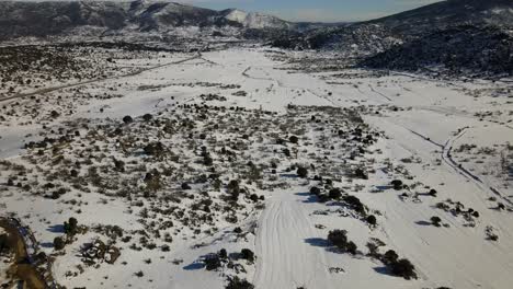 drone flight in reverse focusing on a completely snowy plain with bushes and we visualize a dirt road cleared of snow for access to rural farms with a background of mountains in winter avila spain