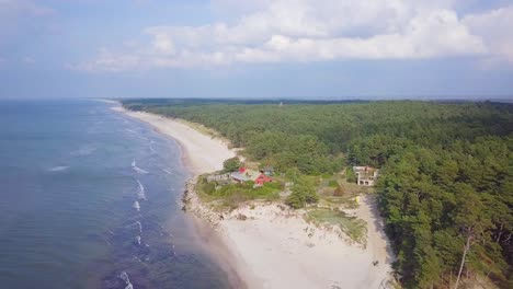 Vista-Aérea-De-La-Costa-Del-Mar-Báltico-En-Un-Día-Soleado,-Dunas-De-Arena-Blanca-A-La-Orilla-Del-Mar-Dañadas-Por-Las-Olas,-Bosque-De-Pinos,-Erosión-Costera,-Cambios-Climáticos,-Nubes-Cumulus,-Tiro-De-Drones-De-Gran-Angular-Moviéndose-Hacia-Atrás