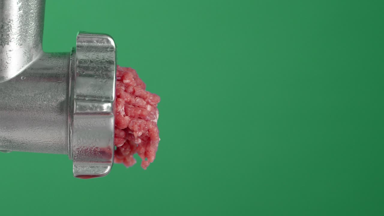 Pieces of raw minced meat fall from the meat grinder.