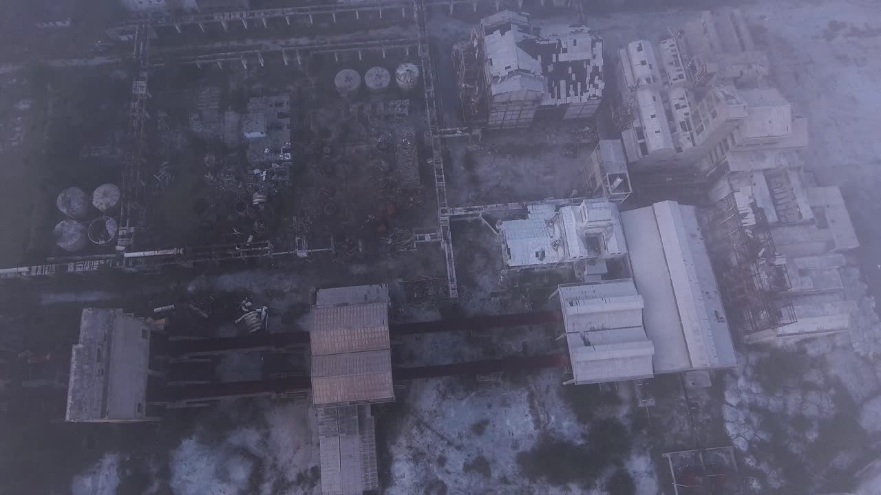 Ruins of a destroyed and creepy factory left abandoned, Drone top down shot above the misty clouds