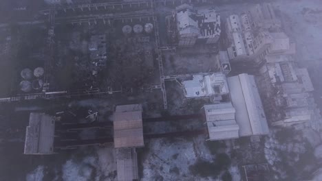 Ruins-of-a-destroyed-and-creepy-factory-left-abandoned,-Drone-top-down-shot-above-the-misty-clouds