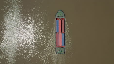 Top-down-view-of-freighter-transporting-shipping-containers-on-a-Southeast-Asian-river