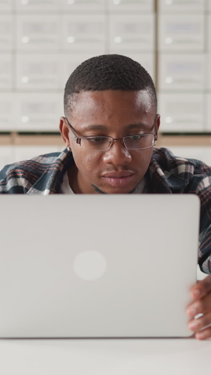 Black man works on laptop in library. African American student studies online information on computer in public library hall. E-learning advantages