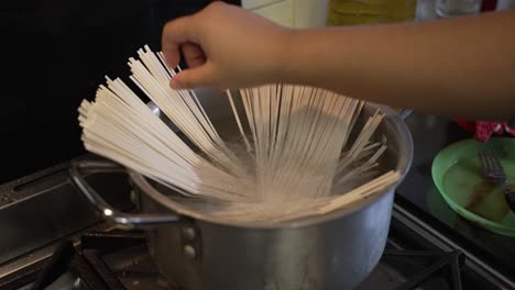 female hand placing raw spaghetti noodles into large pot with water on cooker