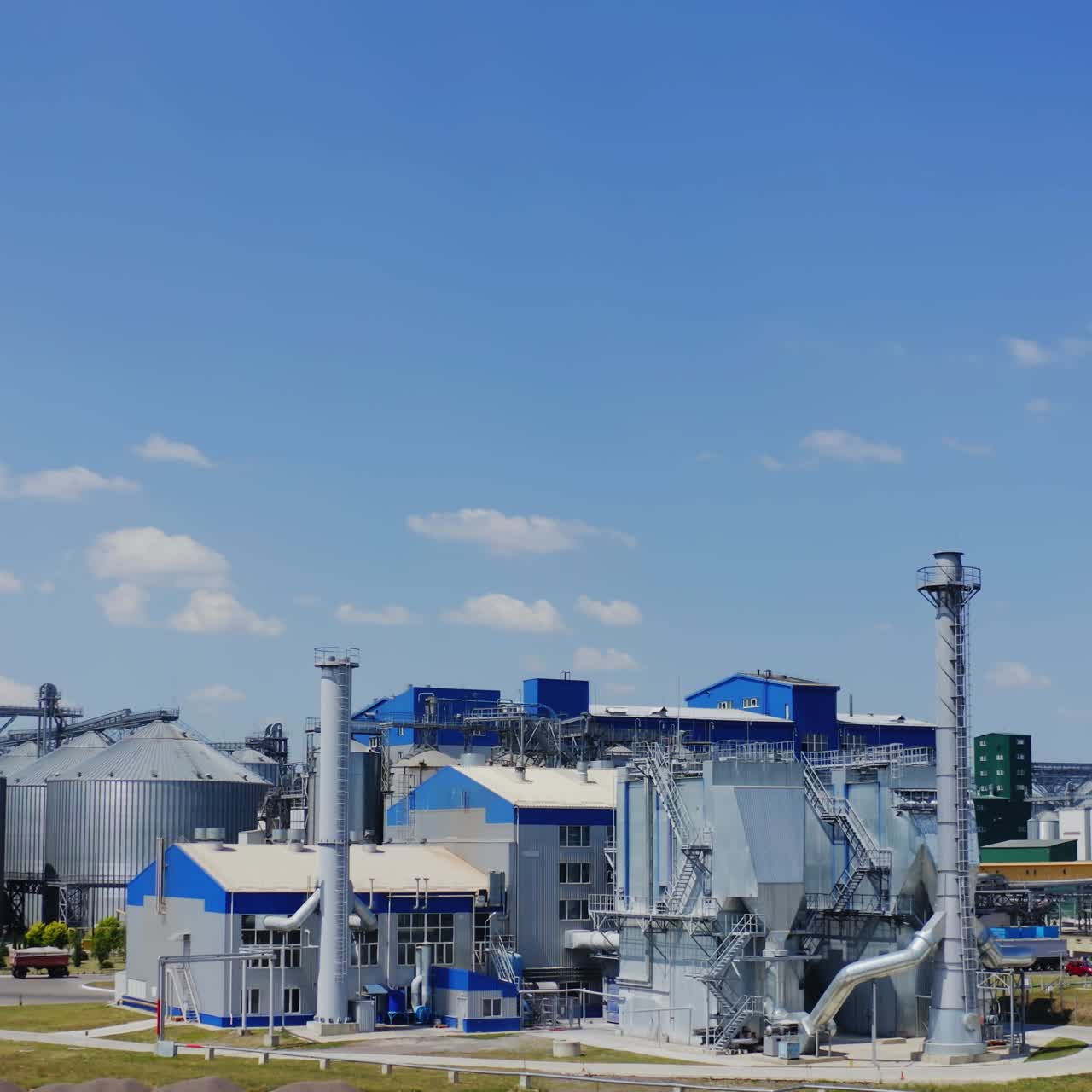 Modern manufacture under blue sky. Grain elevators on field. Industrial zone for storing crop. New architectural buildings of agribusiness. Front view.