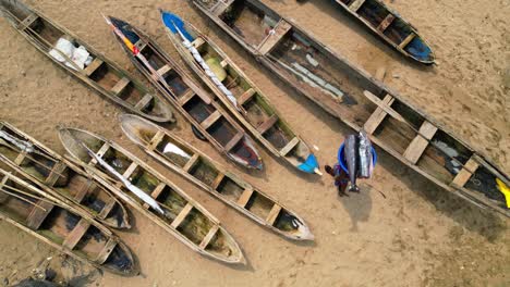top-down aerial view of a woman carrying a swordfish on her head between fishing boats in sao tome, africa