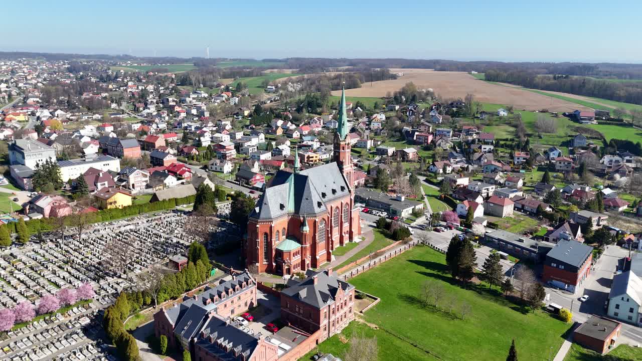 Wide approach over Ludgerovice Saint Mikulase church and surrounding rooftops under soft daylight and blue skies