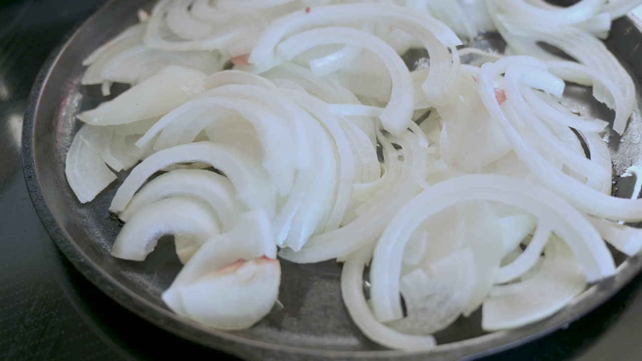 Sliced white onions sauce in oil in cast iron pan on stove, homemade