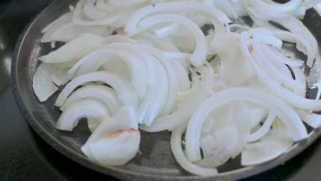 sliced white onions sauce in oil in cast iron pan on stove, homemade