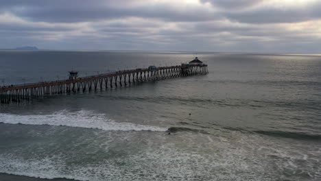 surfers swimming at imperial beach pier in san diego on a cloudy sunset